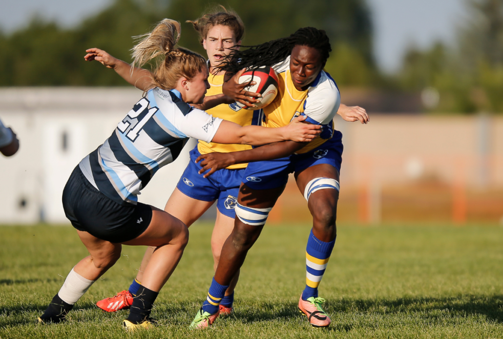 A female rugby player carries the ball away from her opponent