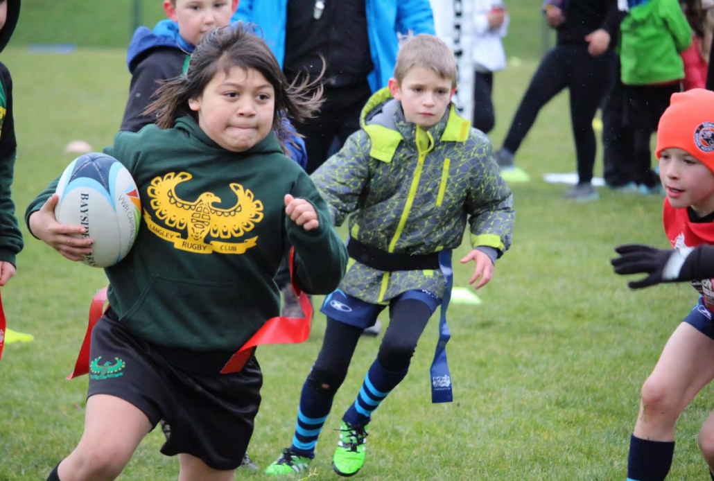 A young girl runs with a rugby ball as other players chase