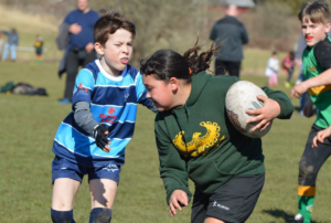 A young girl runs with a rugby ball as two other players chase