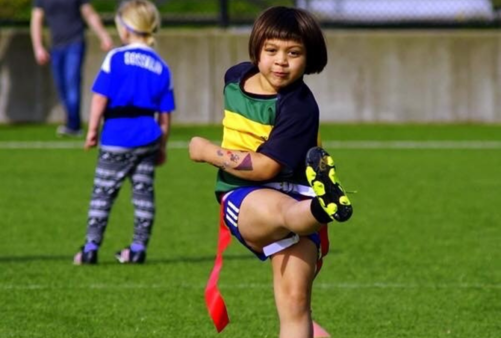 A young girl smiles at the camera as she kicks a Rugby ball