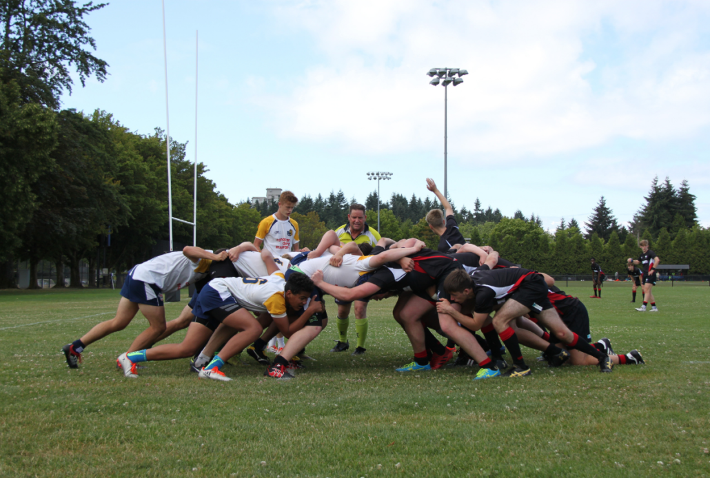 A rugby scrum between two teams takes place on the pitch