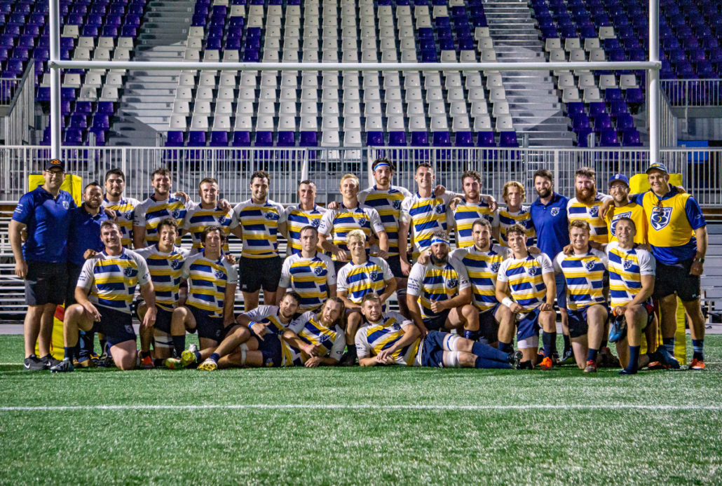A group of male rugby players pose for a photo in front of Rugby posts