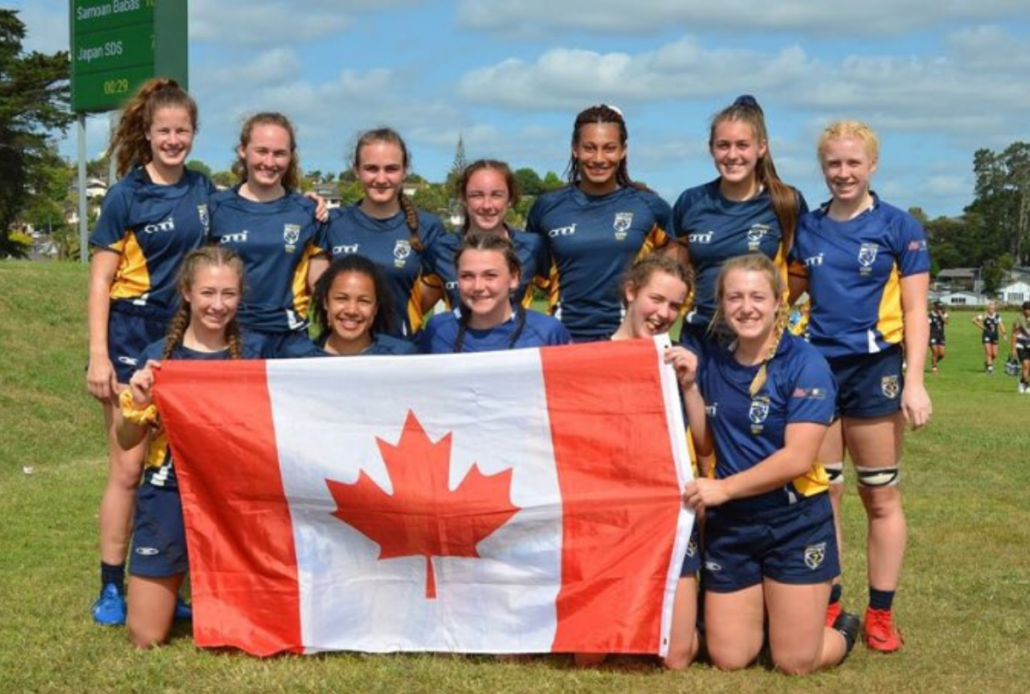 A group of female rugby players pose for a photo with a Canada flag