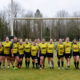 A group of female Rugby players pose for a photo under the posts