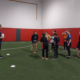 A rugby coach holding a rugby ball talks to a group of young girls during a training session