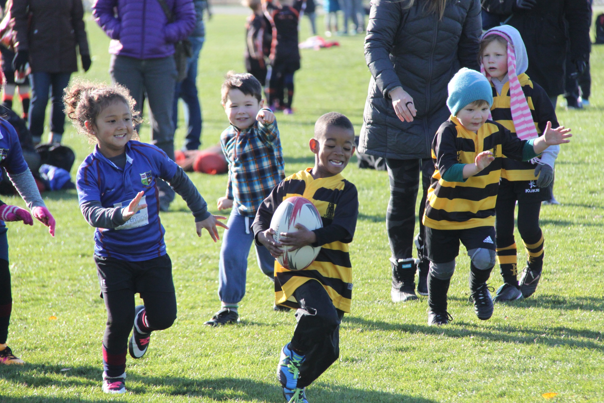A young rugby player runs with the ball as other children chase