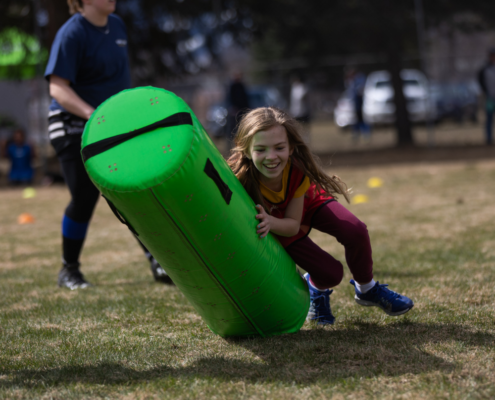 A close up of a girl running on grass and tackling a green tackle bag