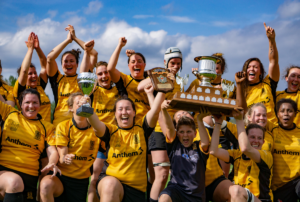 A group of female Rugby players celebrate together with trophies