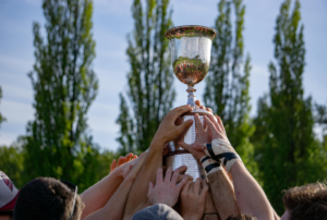 A close up of a team lifting a trophy with a blurred background of trees
