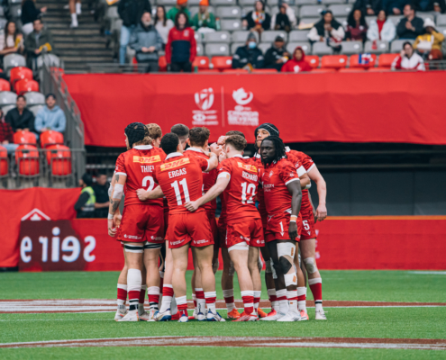 The Canada Men's Sevens team huddles in the centre of the field in BC Place with crowd seen behind