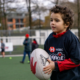 A young boy holds a Rugby ball on a field