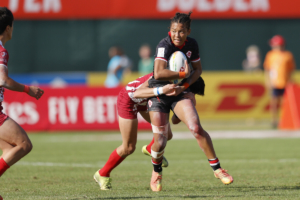 A female Rugby Canada player is tackled from behind while carrying a ball on the field