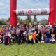 A group of children pose with Rugby Balls under a giant inflatable Rugby goal on grass