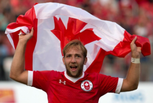 A close up of a man in a red jersey holding a Canadian flag above his head