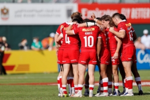 A group of Rugby Canada national team players huddle on a pitch with the background blurred