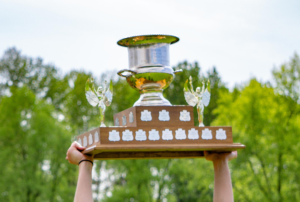 A close up of a cup being lifted above a player's head with trees in the background