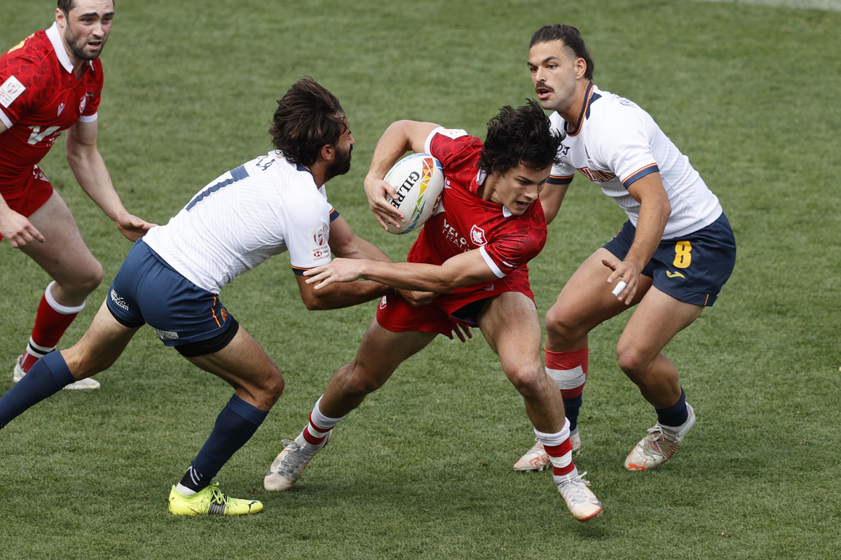 A Canada Men's Rugby Sevens player shields the ball from two opposing players in white shirts