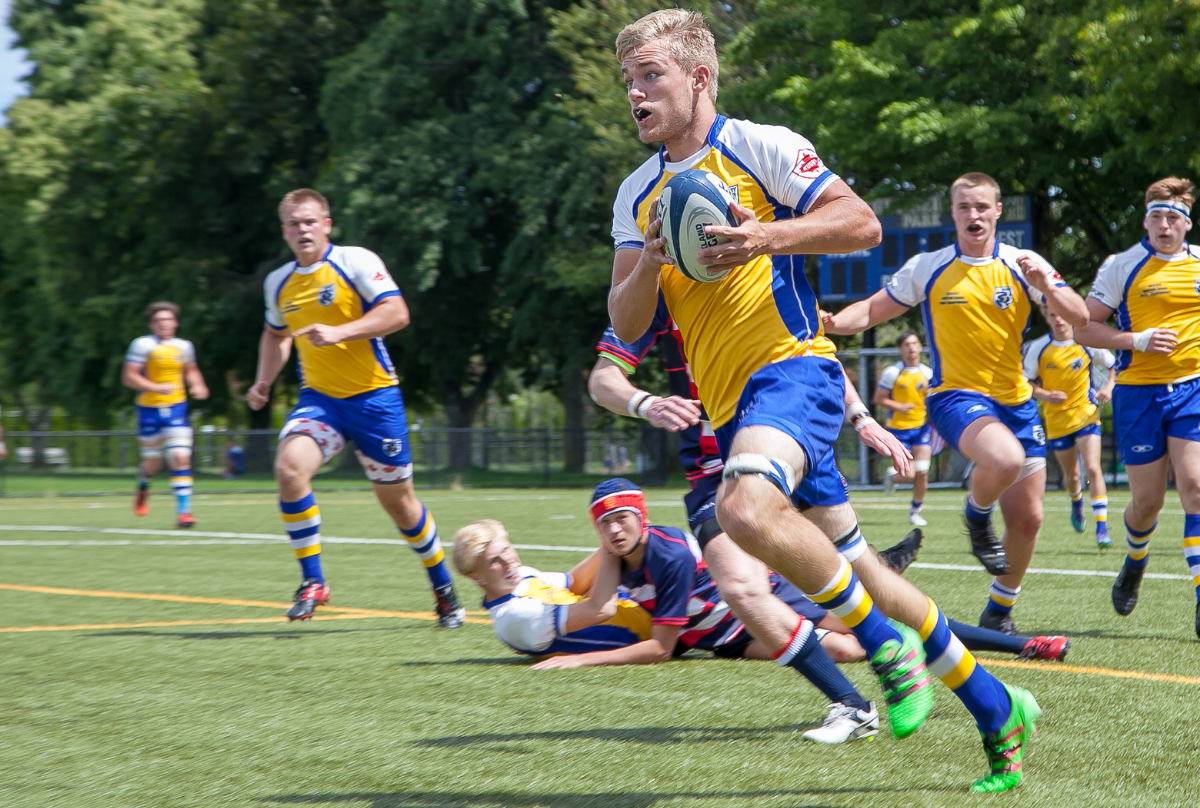 A young male rugby player carries the ball as his team-mates track him