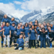 A group of children and Rugby coaches pose smiling in front of Rocky Mountains