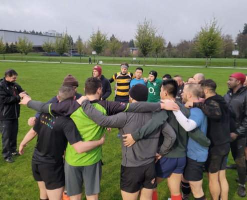 A group of Rugby players huddle while the coach gives a talk on the field