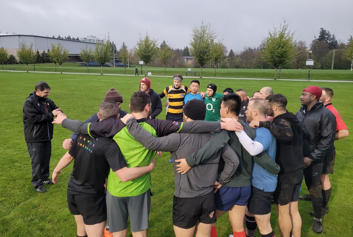 A group of Rugby players huddle while the coach gives a talk on the field