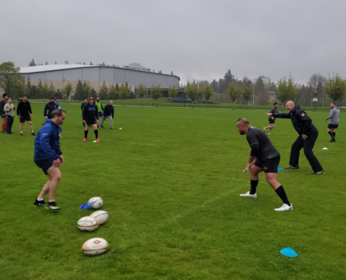A Rugby team runs a passing drill on a field with the Coach pointing instructions
