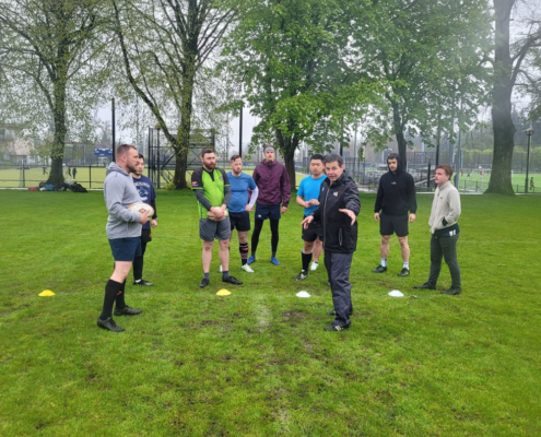 A Rugby coach demonstrates a drill to a group of Rugby players on a field