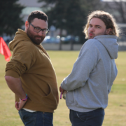 Two male Rugby players pose for a photo by the pitch