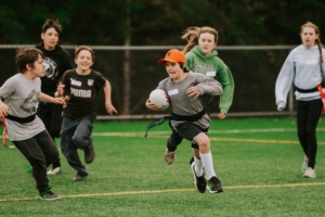 A young rugby player runs with the ball as other children chase