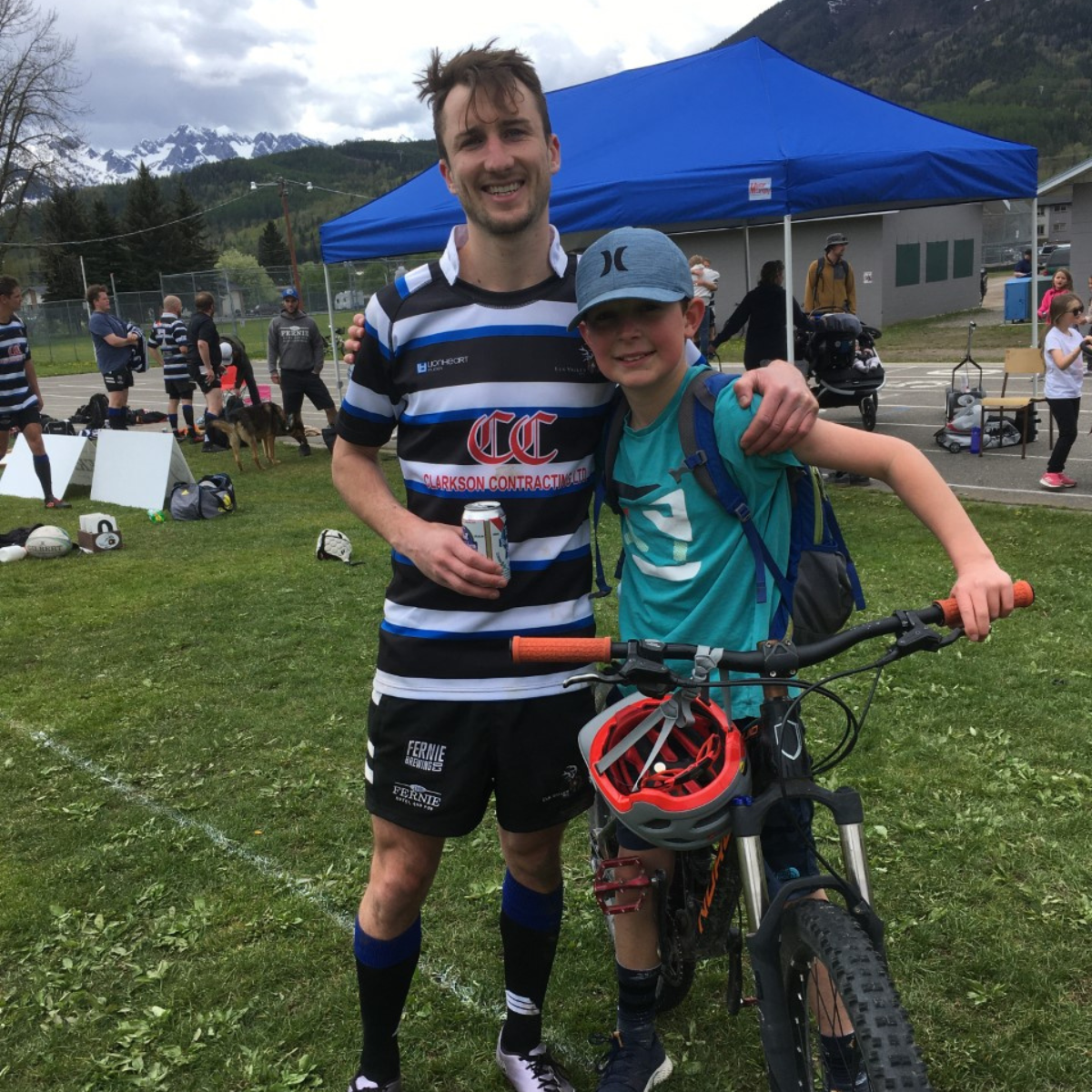Elk Valley Bulls captain Sorla poses with a young boy on a bicycle on the side of a Rugby pitch