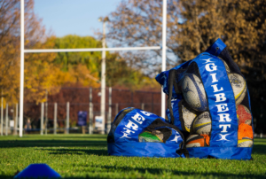 A photo of rugby balls stored in a blue ball bag in front of Rugby uprights