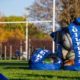 A photo of rugby balls stored in a blue ball bag in front of Rugby uprights