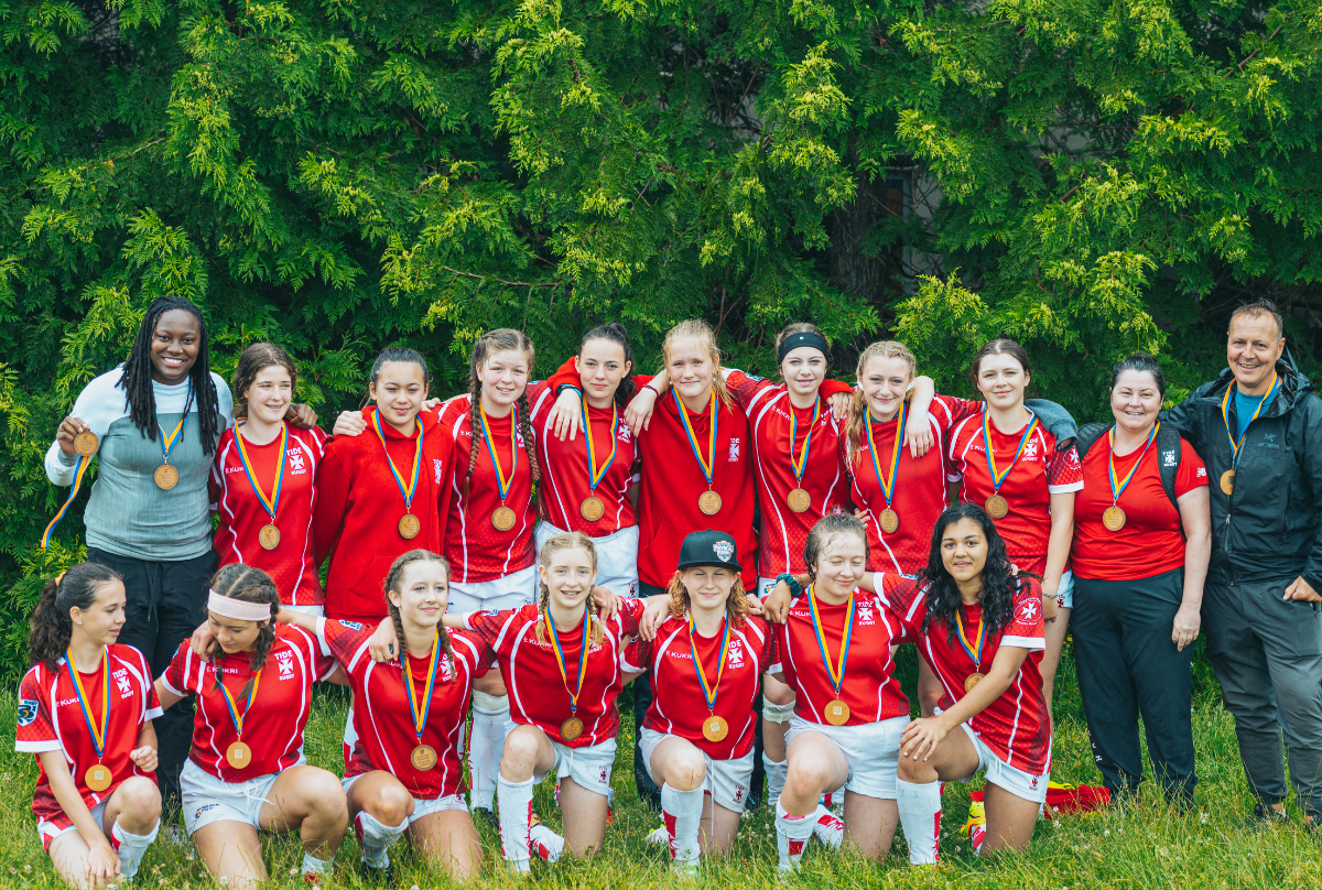 A rugby team of junior girls in red jerseys pose with medals after a match