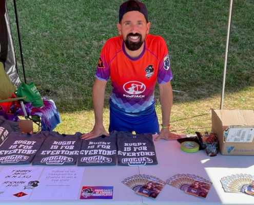 A Vancouver Rogues player sells merchandise at a booth during 2022 Vancouver Pride Festival