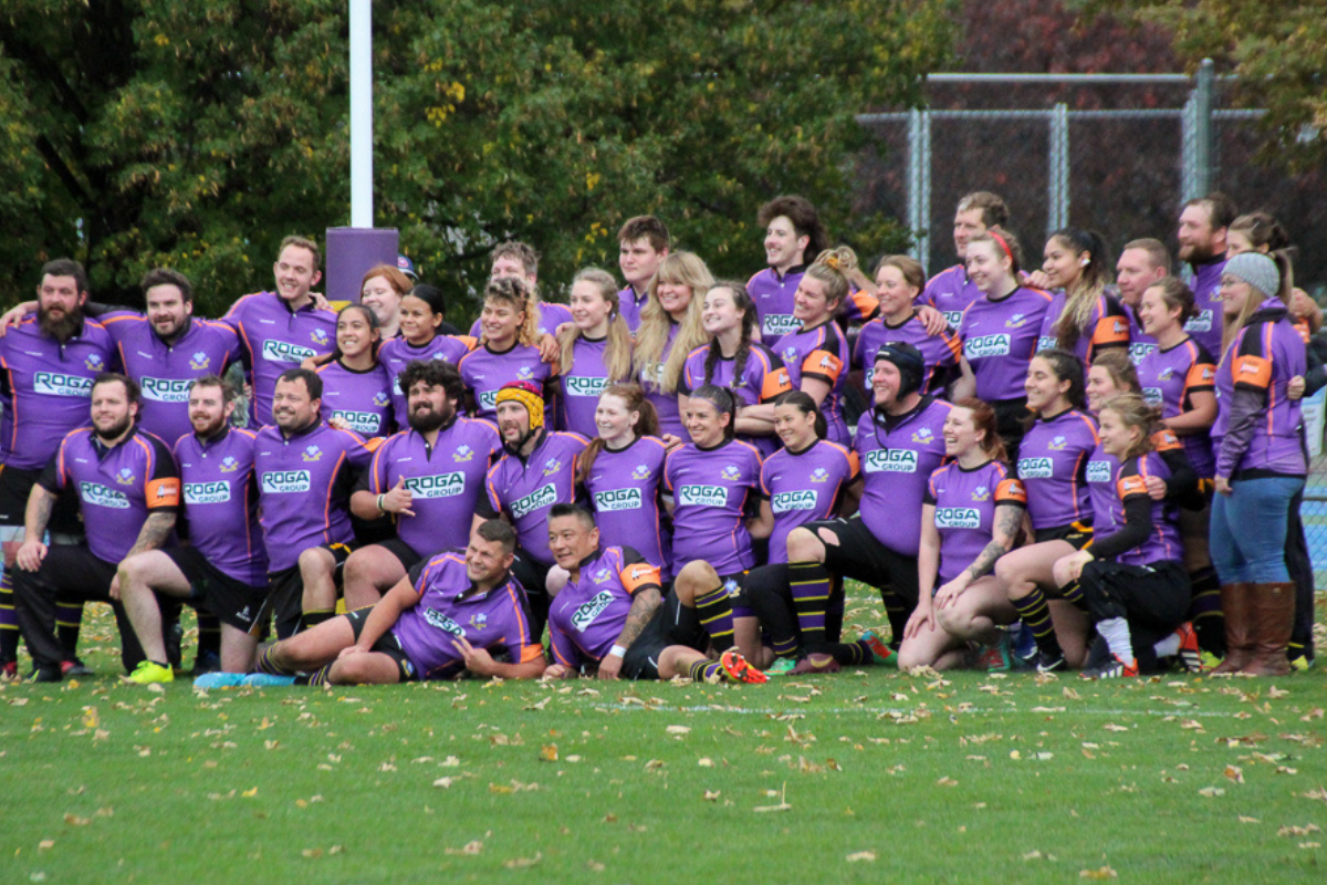 A group of male and female rugby players pose for a team photo under the posts