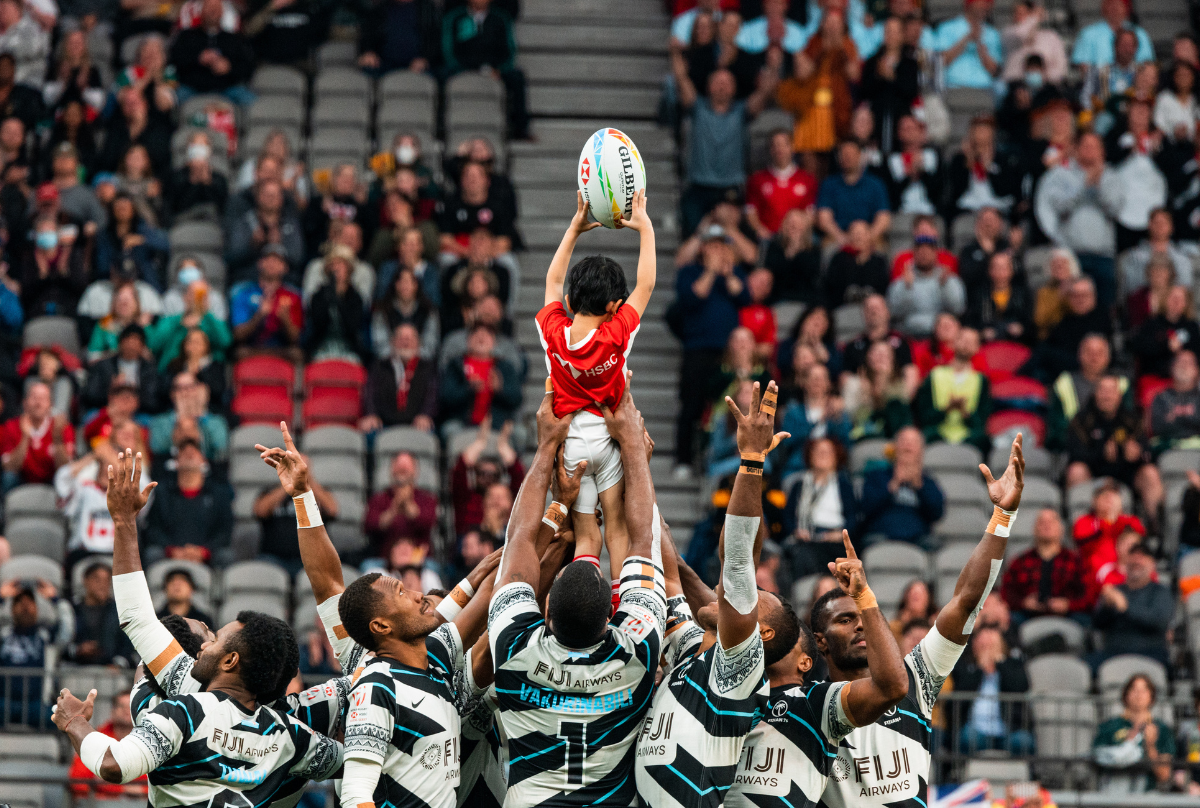 A HSBC Rookie Rugby Ball Carrier is lifted into the air by the Fiji Men's Sevens team after delivering the match ball onto the BC Place Field