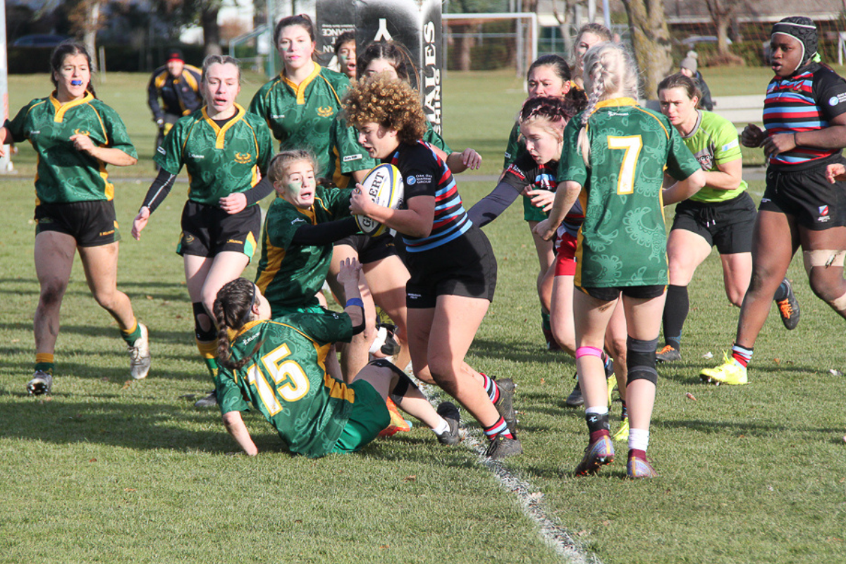 A player runs with a rugby ball and evades several challenges from opposition
